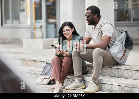 Portrait of two young business people chatting while sitting on steps in city, copy space Stock Photo