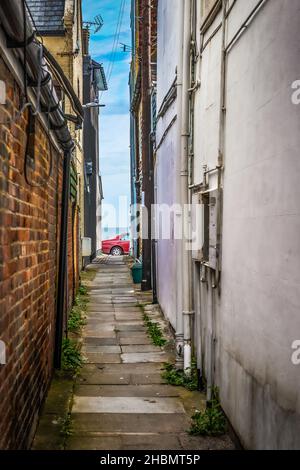 Looking down an empty narrow alleyway towards a red parked car and the sea in the background, taken at Sandgate near Folkestone 26th June 2021 Stock Photo