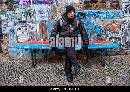 Elderly senior man sits on bench outside dilapidated graffiti-covered squat building, Linienstrasse 206,Mitte,Berlin Stock Photo