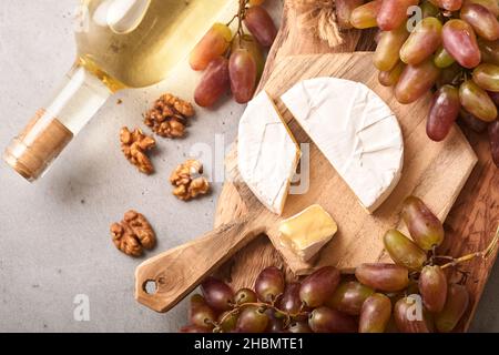 Two Wine bottles with grapes, slice cheese camembert, nut and wineglasses on old gray concrete table background with copy space. Red wine with a vine Stock Photo