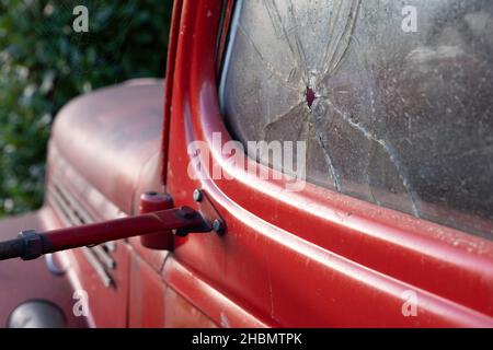 Side view of old mid 20th century red Pick Up with a bullet hole and crack in the car window door. Focus on the bullet hole at the right Stock Photo