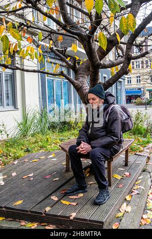 Elderly senior man sitting on a  bench in autumn - Schulzestraße, Pankow, Berlin. Thoughtful, looking pensive Stock Photo