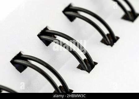 Macro photo of a white notebook with a black metal spiral connecting the pages. Stock Photo