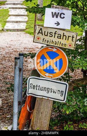 Several signs – WC, keep exit clear, no stopping, and emergency access route – are stacked on a post beside a path in the Stubai valley. Stock Photo