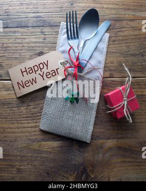 New years eve meal table setting, greeting card attached to fork and knife on wooden table Stock Photo