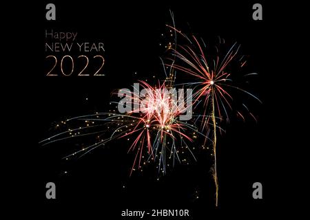 Happy New Year 2022 text and exploding colorful fireworks rockes against a black night sky, copy space