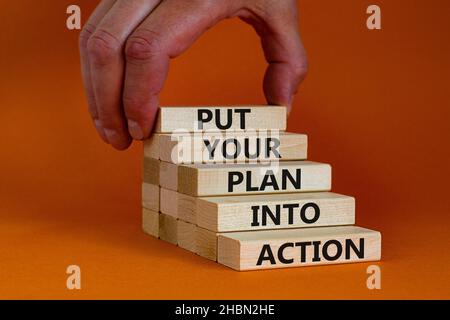 Put your plan into action symbol. Wooden blocks with words Put your plan into action. Beautiful orange background, copy space. Businessman hand. Busin Stock Photo