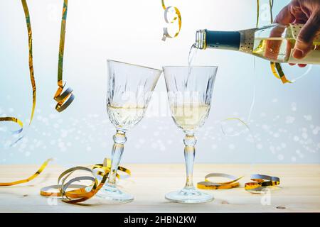 Pouring champagne from a bottle in two glasses to toast for new year or other celebrations, festive golden streamers against a light background, selec Stock Photo