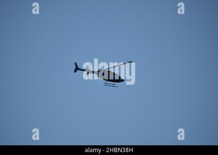 Side view of a helicopter tilting away against a clear blue sky. Stock Photo