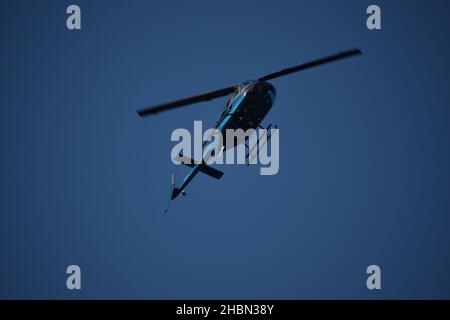 Bottom view of blue helicopter flying overhead. Stock Photo