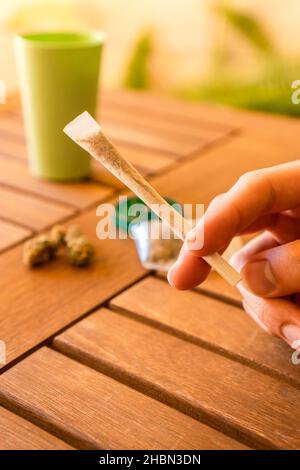 Close up of hand with cannabis joint in an outdoor and brightness location with plants. Stock Photo