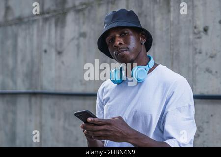 A closeup of a man with white t shirt and a blue headset standing in the street and using phone, Spain Stock Photo