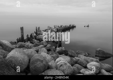 an old pier made of stones and wooden legs is left with metal screeds and the water surface is calm Stock Photo