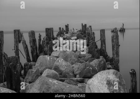 an old pier made of stones and wooden legs is left with metal screeds and the water surface is calm Stock Photo