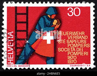 SWITZERLAND - CIRCA 1970: a stamp printed in the Switzerland shows Fireman Rescuing Child, Centenary of the Swiss Firemen’s Association, circa 1970 Stock Photo