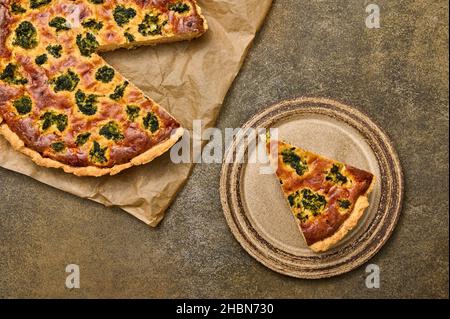 Piece of quiche tart on ceramic rustic plate. Nearby is large pie on parchment paper. Top view Stock Photo