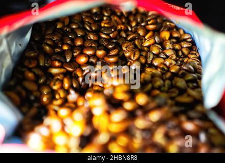 Brown glowing coffee beans in a horizontal red bag, selective focus Stock Photo