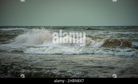 waves in the sea with white foam in the evening at sunset, but the sun is hidden behind the clouds Stock Photo