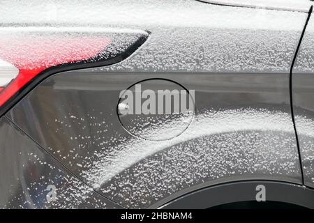 Grey car after snowfall side view partially red headlamp and round cover from gas tank close up. Light passenger car luxury class under snow cover. Stock Photo