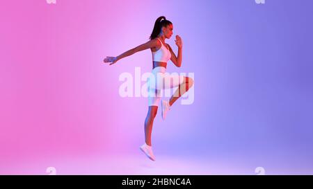 Woman Doing Elbow-To-Knee Crunch Standing Over Pink And Blue Background Stock Photo
