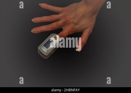 A woman performs her own pulse oximetry and saturation levels at home using a pulse oximeter. Stock Photo