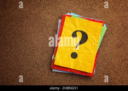 A stack of colorful paper notes with question marks on them on a cork board. Close up. Stock Photo