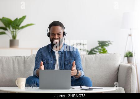 Glad friendly young african american bearded businessman in headset work on computer on sofa Stock Photo