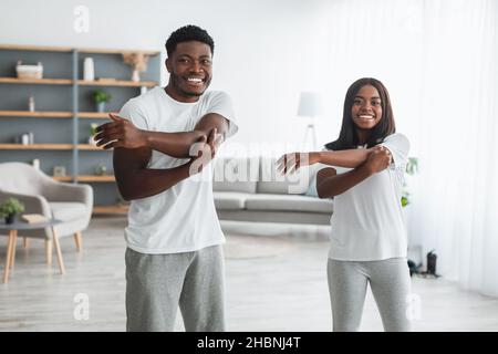 Young black couple doing arm stretch exercise together at home Stock Photo