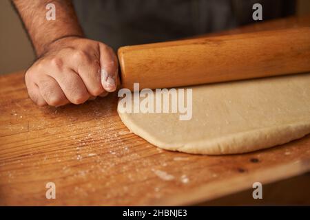 hands of a cook on his rolling pin stretching a dough Stock Photo