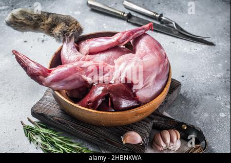 Raw hare game meat, legs and offals in wooden plate with herb. Gray background. Top view Stock Photo