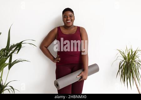 Photo of cheerful overweight black lady with fitness mat Stock Photo