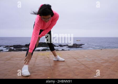 Young woman performs stretching exercises in front of the sea. sport Stock Photo