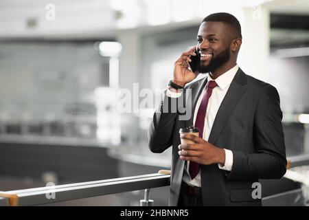Cheerful black manager drinking coffee, having phone conversation Stock Photo