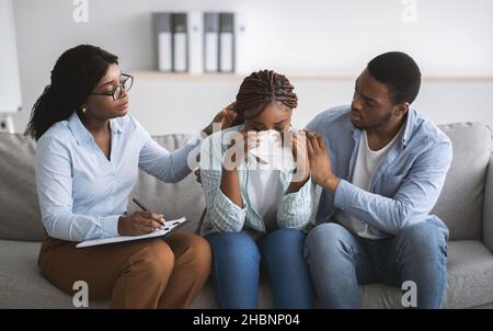 Millennial lady crying on session with marital counselor at office, affectionate husband comforting her Stock Photo