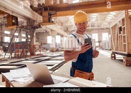 Cheerful builder using smartphone at construction site Stock Photo