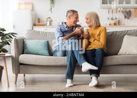 Happy Senior Couple Drinking Coffee Holding Mugs Sitting At Home Stock Photo