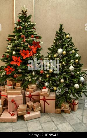 Two pine trees with white, red and yellow balls, pine cones, a garland of poinsettia flowers and wrapped in paper gifts with a red ribbon lying under Stock Photo