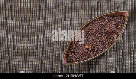 Black mustard seeds in wooden bowl - Brassica nigra Stock Photo