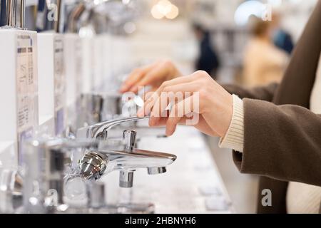 Men's hands in a brown coat choose a water mixer in a construction supermarket, close-up Stock Photo