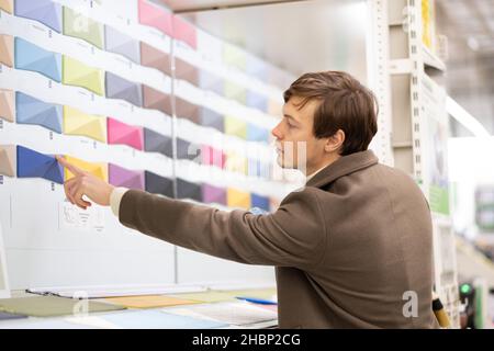 business man in brown coat chooses paint tile color on color palette at hardware store Stock Photo