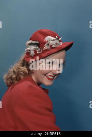 Portrait of young woman in red coat and hat sitting sideways Stock Photo
