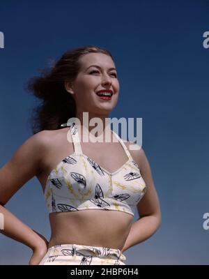 Young woman in white 2-piece bathing suit hands on her hips gazing out Stock Photo