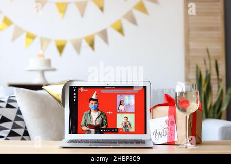 Laptop, gift and glass of wine on table in room. Celebrating Birthday online due to coronavirus epidemic Stock Photo