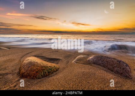 A Beautiful Colorful Ocean Sunset As The Moon Rises In The Sky And A Wave Crashes On The Sandy Seashore Stock Photo