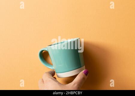 Hand holding mint green mug cup on orange background. top view, copy space Stock Photo