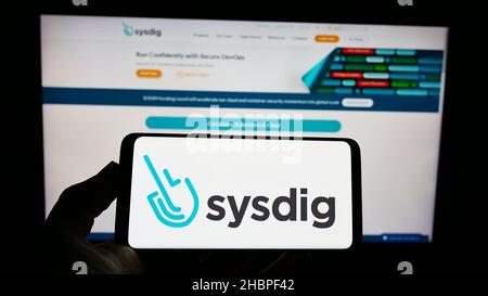 Person holding smartphone with logo of US cloud security company Sysdig Inc. on screen in front of website. Focus on phone display. Stock Photo