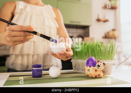 Soft selective focus. Child's hands paint Easter egg with artistic brush on blurred background of home interior. do-it-yourself. Hobby with paints. Stock Photo