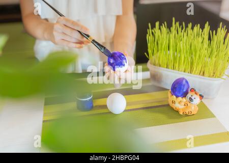 Soft selective focus. Child's hands paint Easter egg with artistic brush on blurred background of home interior. do-it-yourself. Hobby with paints. Stock Photo