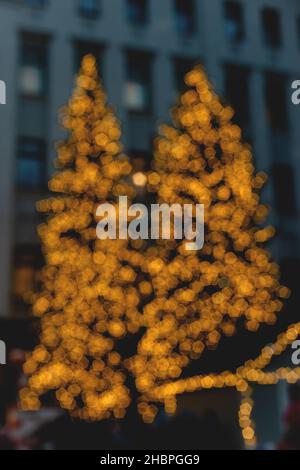 Christmas trees in christmas light garland on background of multi storey building. Blurred image. Wallpaper Stock Photo
