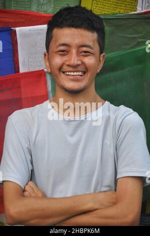Waist up of a happy Ladakhi guy posing with crossed hands looking at camera, standing against Tibetan prayer flags Stock Photo